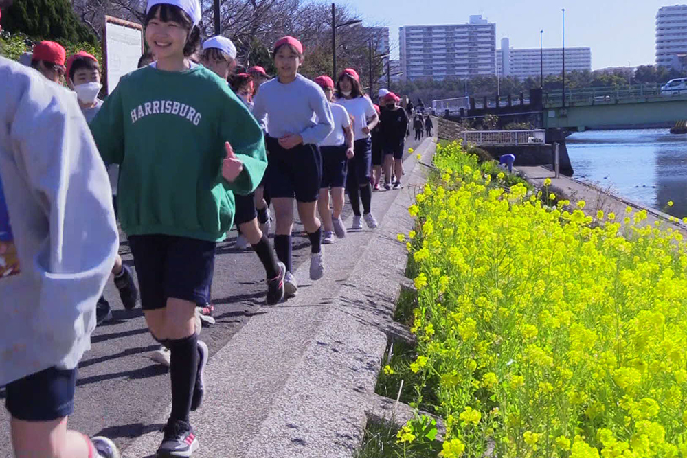 満開の菜の花の横を笑顔でランニング